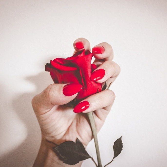 Elegant red gel nails holding a delicate flower at River Cottage Beauty Salon, Hamstreet, Kent – professional nail treatment with a glossy, long-lasting finish